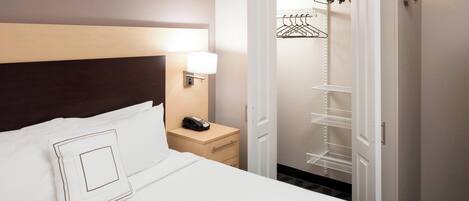 A hotel room with a bed, a bedside table with a lamp, a phone, and a closet with shelves.