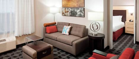 A hotel room with a sofa, a small table, a lamp, a bed, and a nightstand.