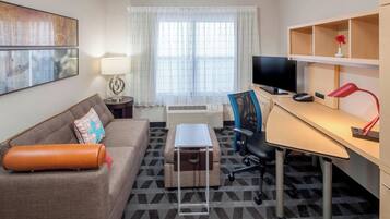 A hotel room with a sofa, a desk with a computer, a TV, and a lamp.