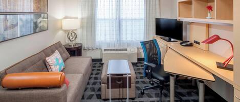 Ein Hotelzimmer mit einer Couch, einem Schreibtisch mit Computer, einem Fernseher und einer Lampe.