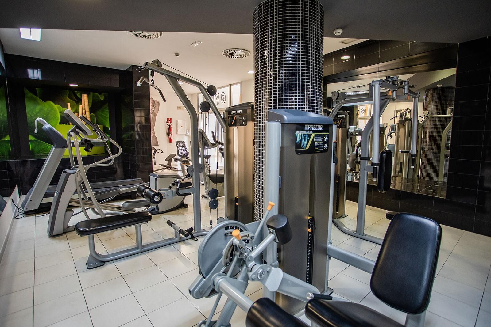Un gimnasio con diversos equipos de ejercicio, incluyendo una máquina de prensa de piernas y una banca.