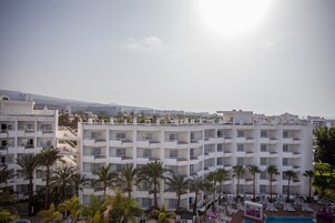 Un hotel con diversi piani, balconi e una zona piscina con lettini.