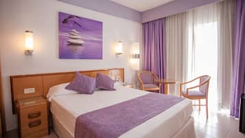 Una habitación de hotel con una cama, dos mesitas de noche, una silla, una pequeña mesa y un cuadro en la pared.