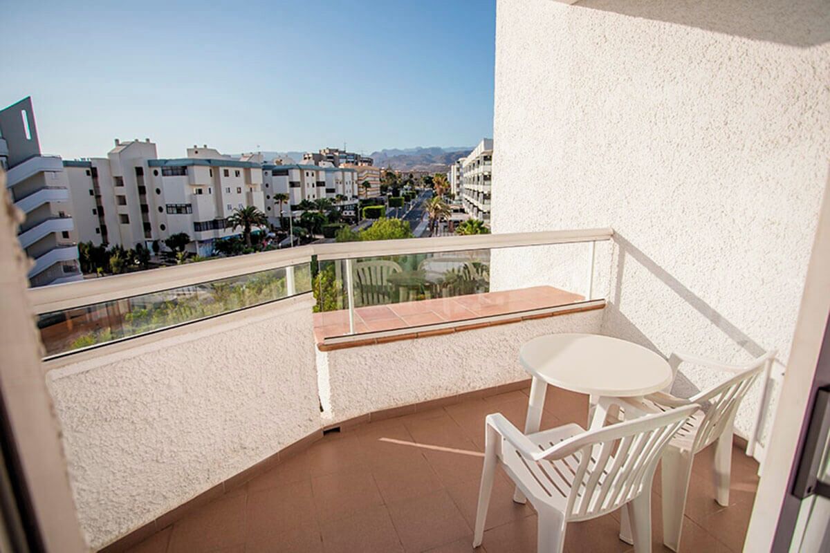 A balcony with a glass railing, a white table, and two white chairs.