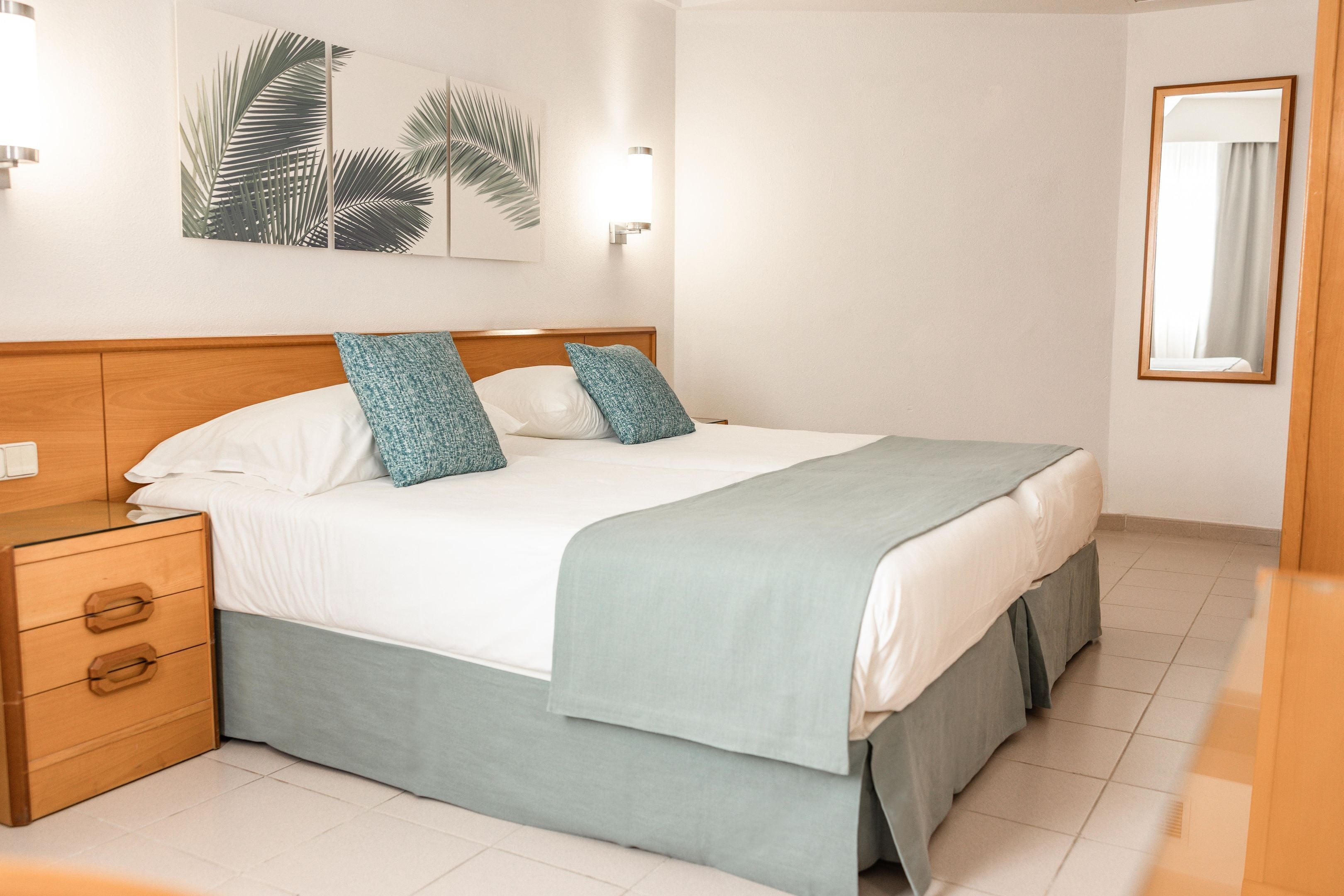 A neatly made bed with a wooden headboard, a bedside table with drawers, and a wall-mounted light fixture.