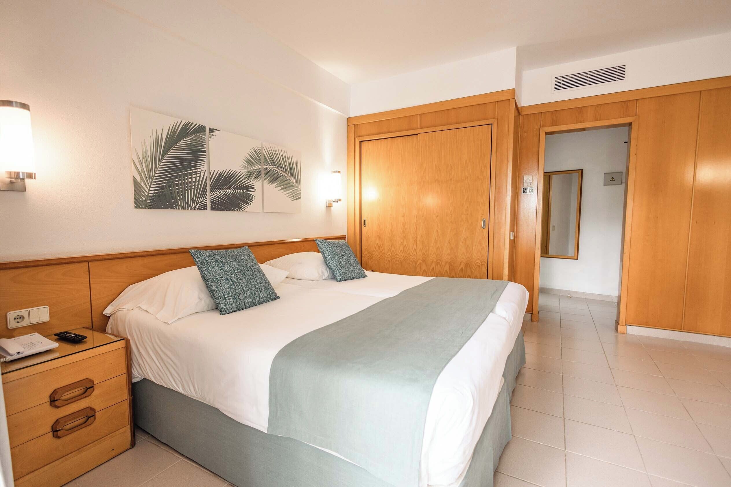 A neatly made bed with a white and light blue bedspread, two pillows, and a bedside table with a lamp and a phone.