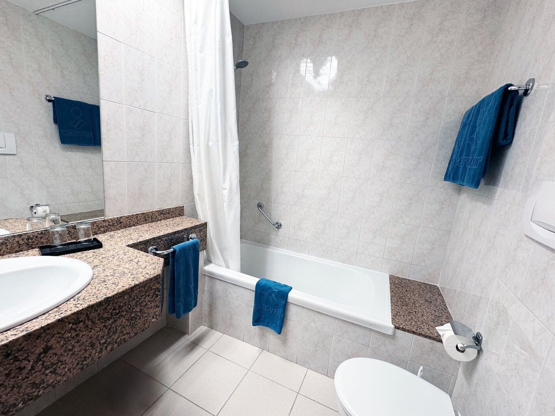 Un baño moderno con encimera de granito, un lavamanos blanco, una bañera y un inodoro.