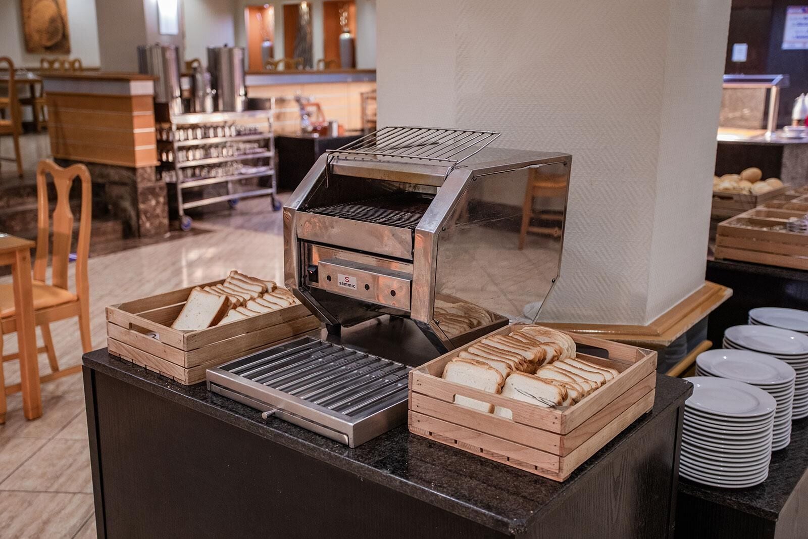 A breakfast buffet setup with a coffee machine, wooden bread baskets, and stacked plates.