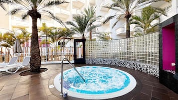 Een jacuzzi omringd door palmbomen en ligstoelen in een hotelatrium.