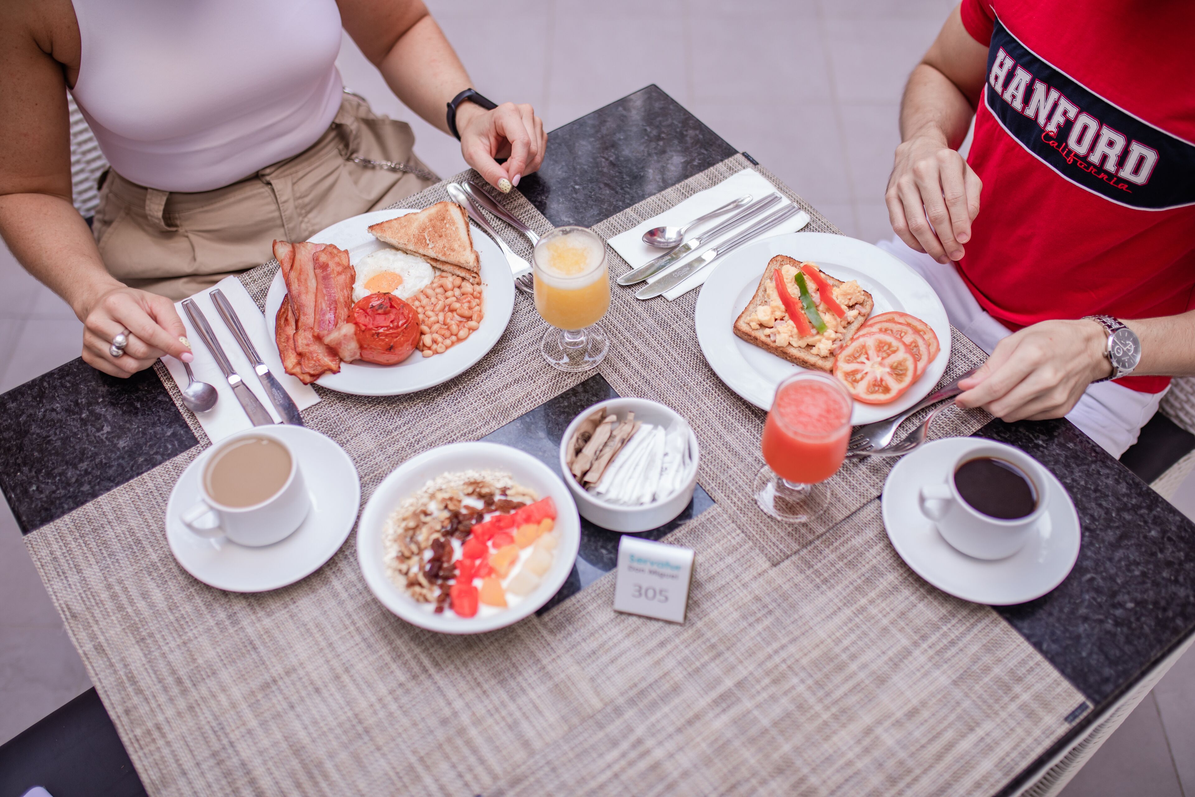 A breakfast table with plates of toast, eggs, bacon, and fruit, along with cups of coffee and juice.