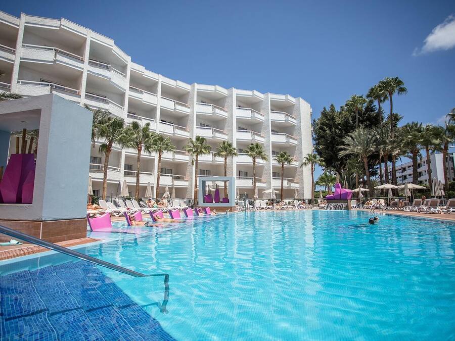 Un hotel con una piscina amplia, varios balcones y palmeras.