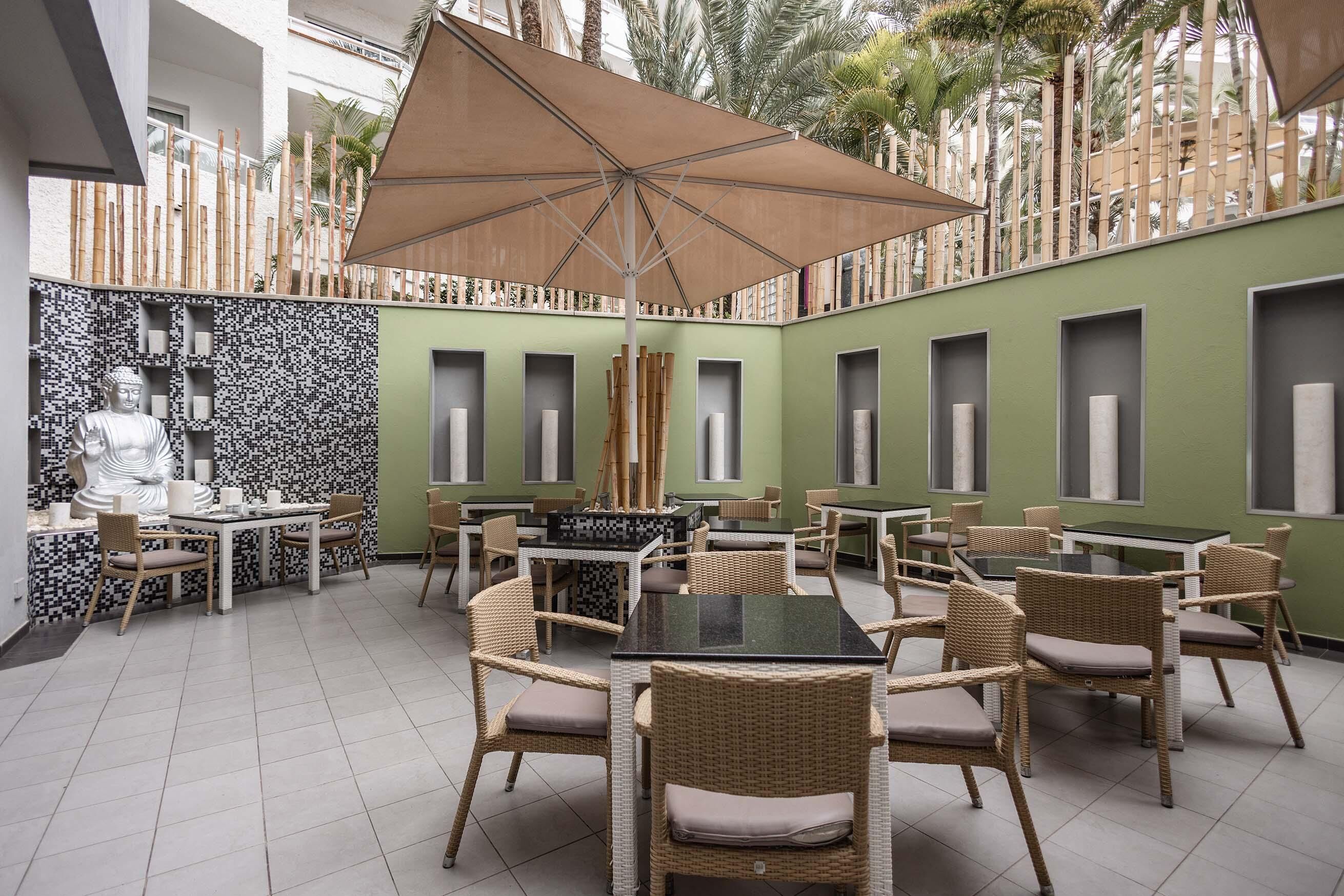 Un restaurante con mobiliario de mimbre, paredes verdes y un paraguas grande.