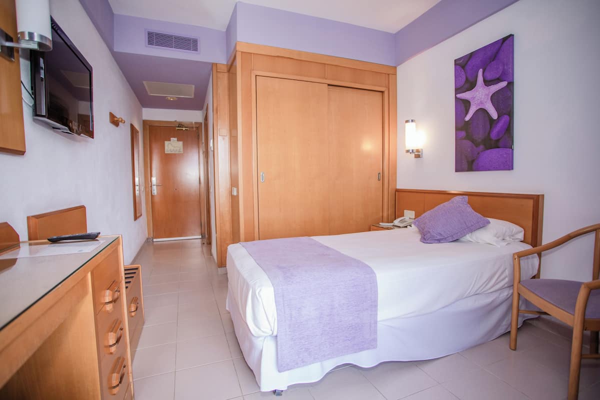 A hotel room with a bed, a desk with a chair, a wardrobe, and a television on the wall.