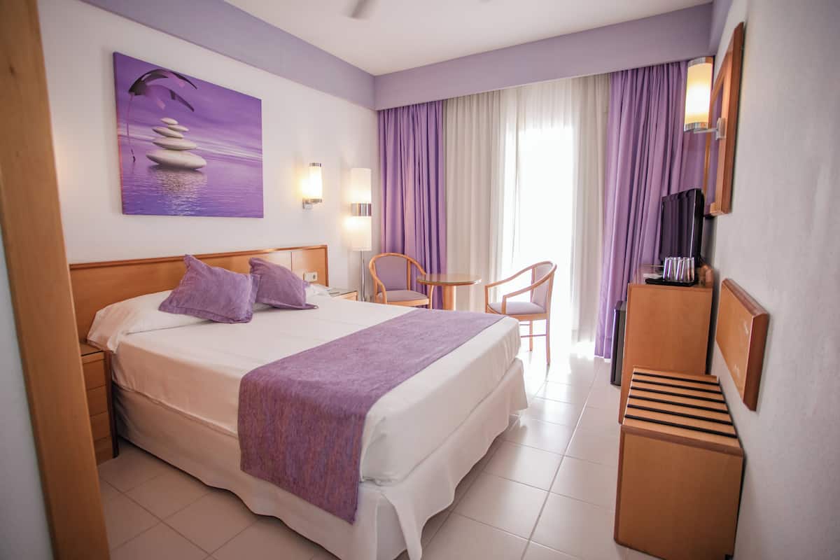 A hotel room with a bed, a desk, a chair, a TV, and a painting on the wall.