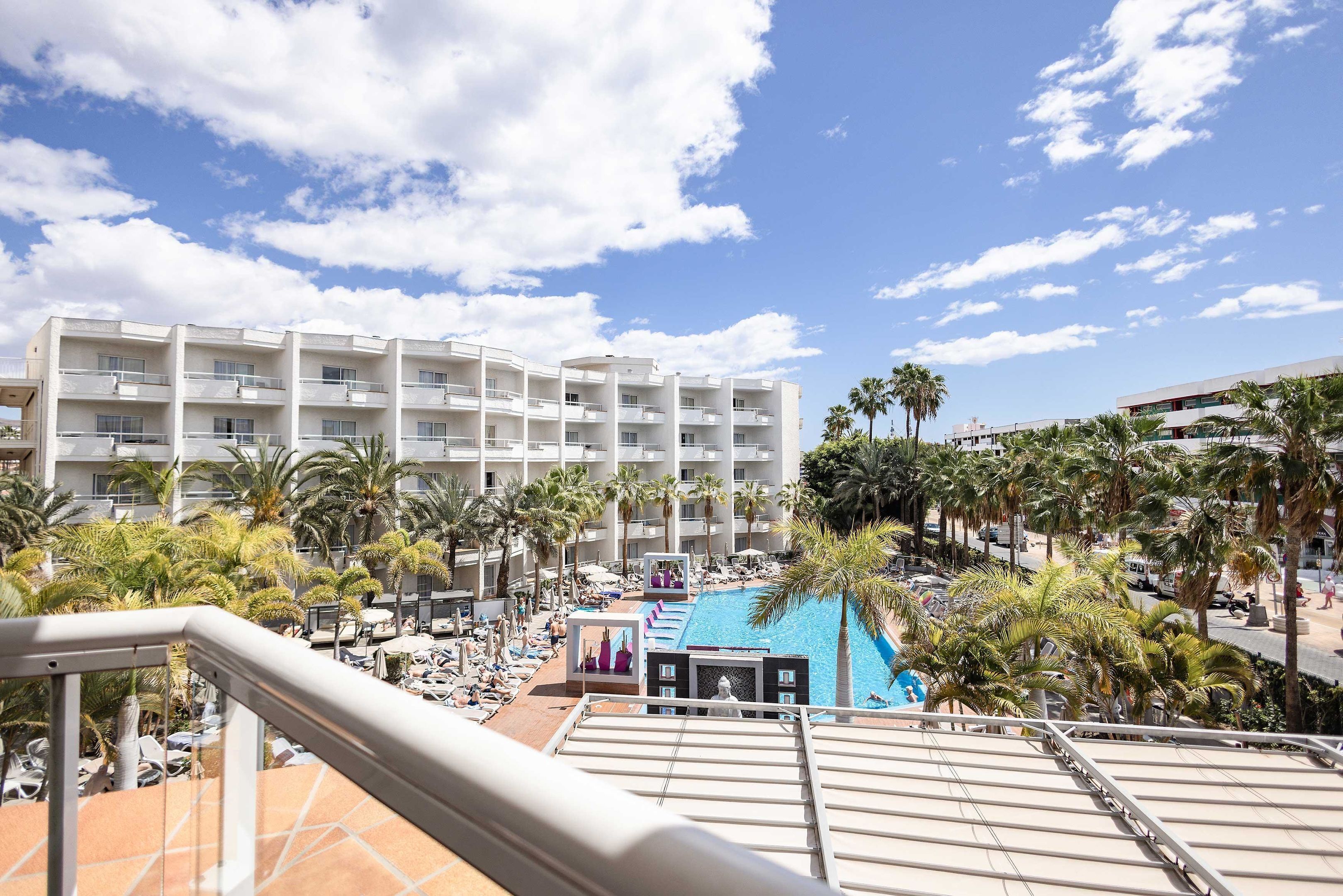 A hotel with multiple floors, a pool area, and palm trees.