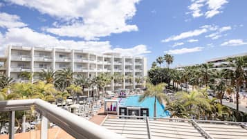 Un hotel con varias plantas, zona de piscina y palmeras.