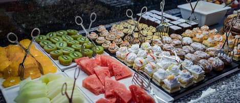 Una presentación de diversos postres y frutas, como sandía, kiwi y pastelería, dispuesta en platos con utensilios de servir.