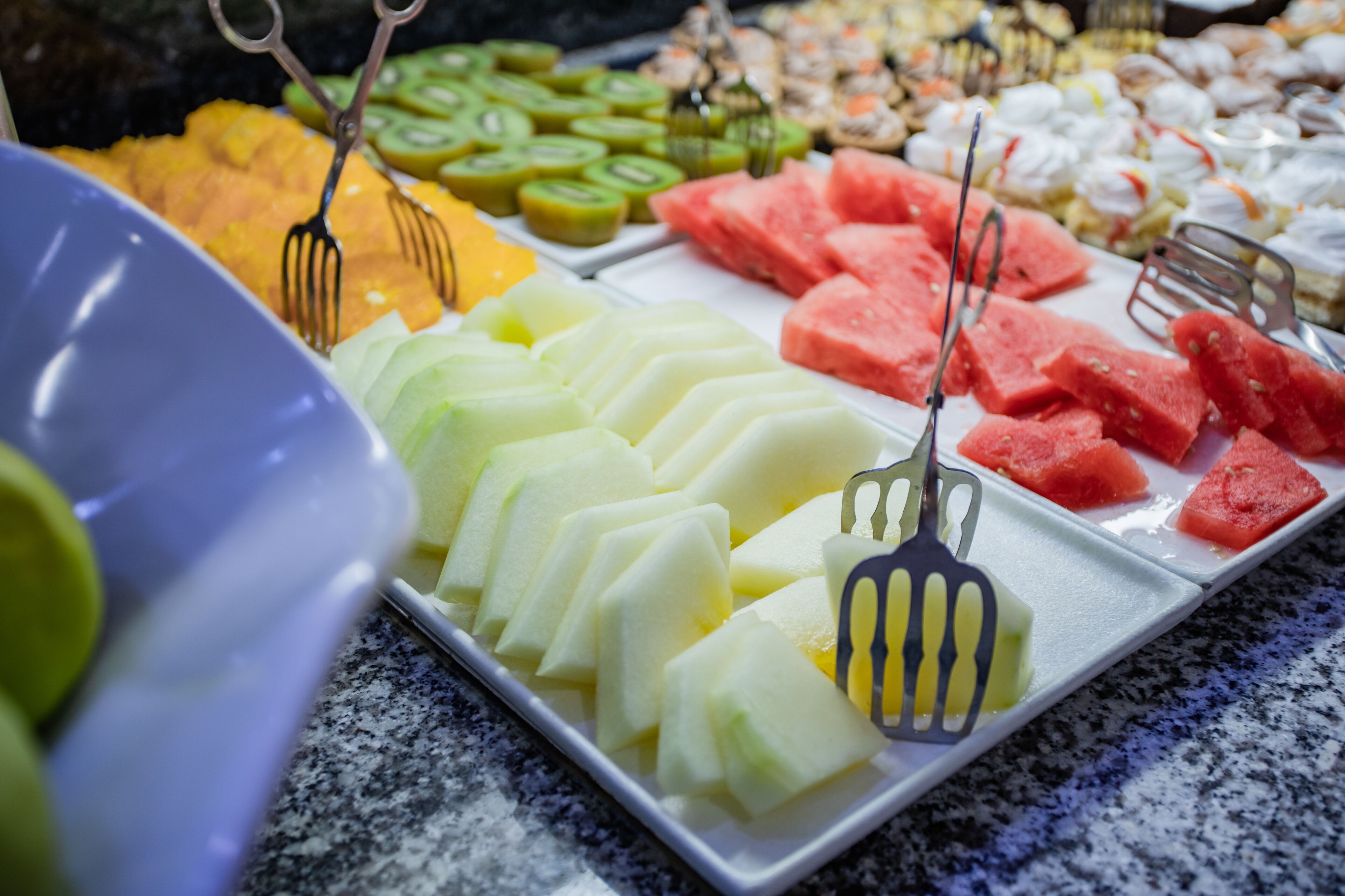 Un buffet con diverse varietà di frutta e verdura, tra cui anguria, kiwi e fette di melone.