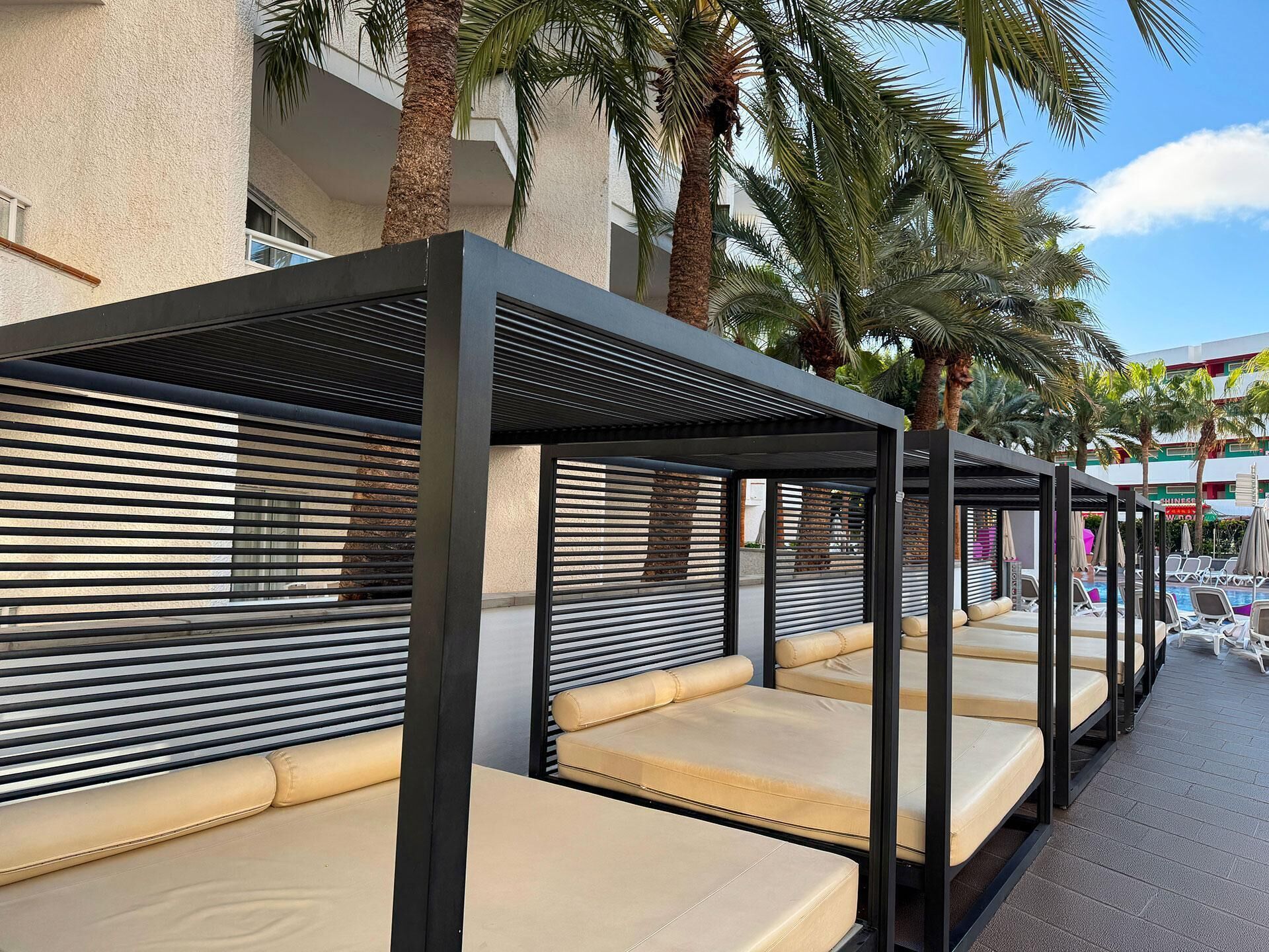 Outdoor seating areas with metal railings and cushioned benches, surrounded by palm trees and a pool.