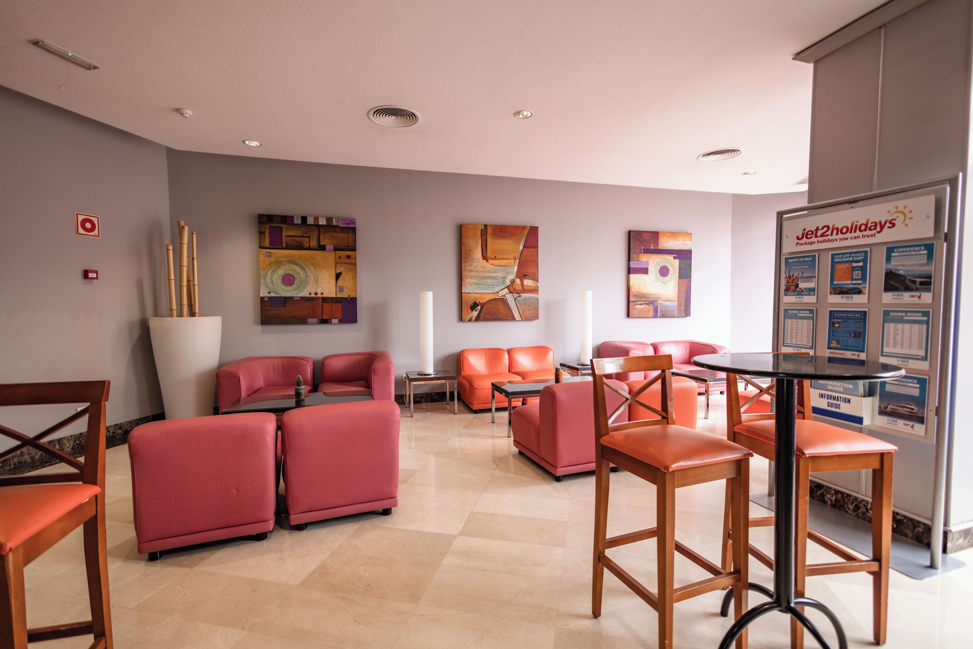 A modern hotel lobby with red seating, artwork on the walls, and a Jet2 holidays information board.