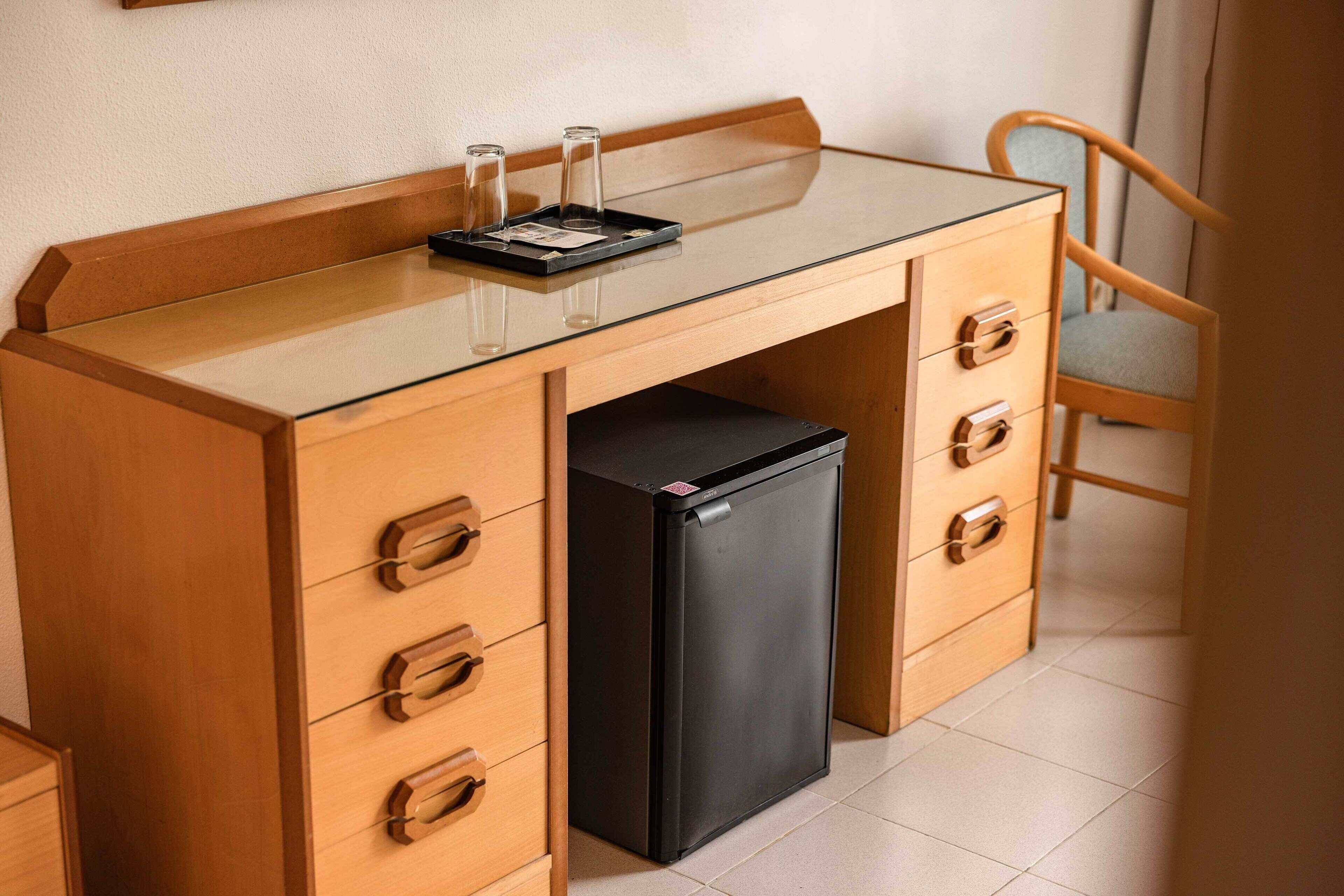 Une petite cuisine équipée avec un plan de travail en verre, un réfrigérateur noir et des meubles en bois dotés de tiroirs.