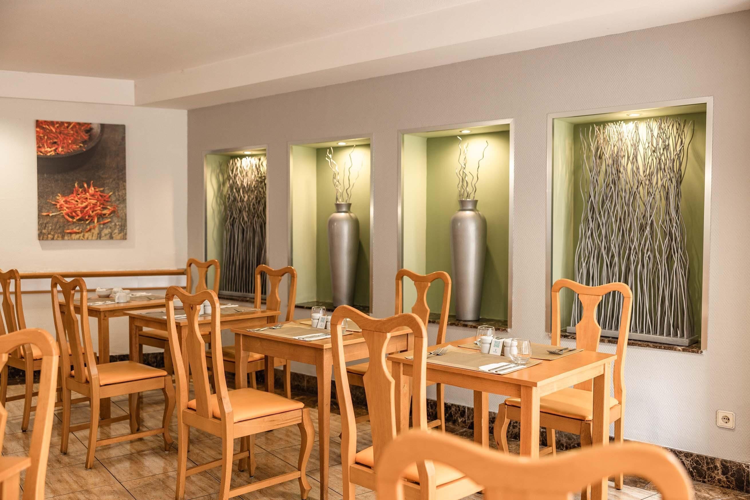 A dining area with wooden tables and chairs, a painting on the wall, and decorative vases with light fixtures.