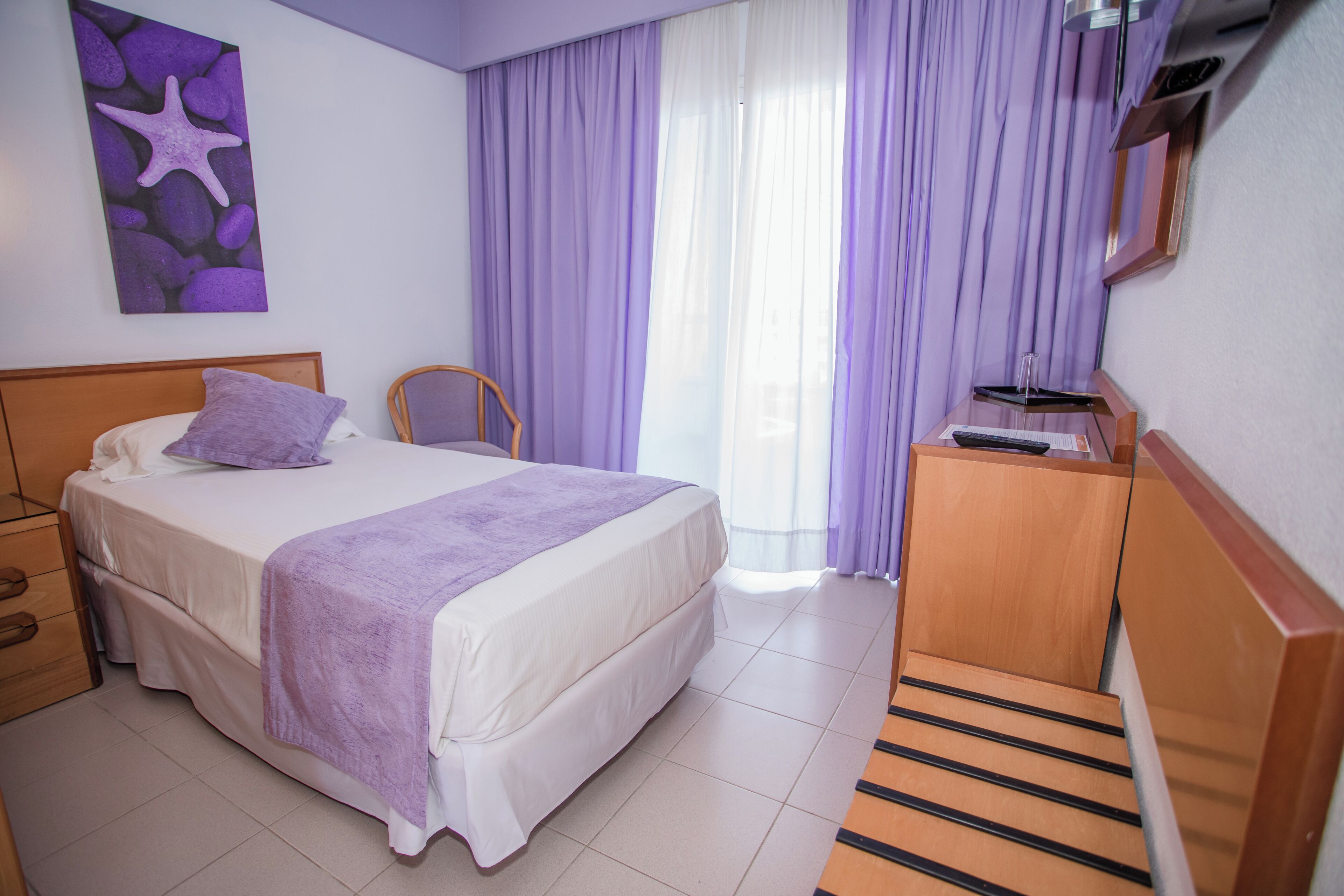 A bedroom with a bed, a chair, a desk, and a starfish artwork on the wall.