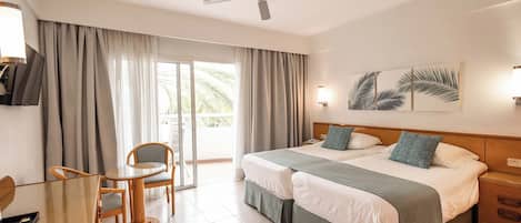 A hotel room with a bed, a desk with a chair, a ceiling fan, and a view of the outdoors.