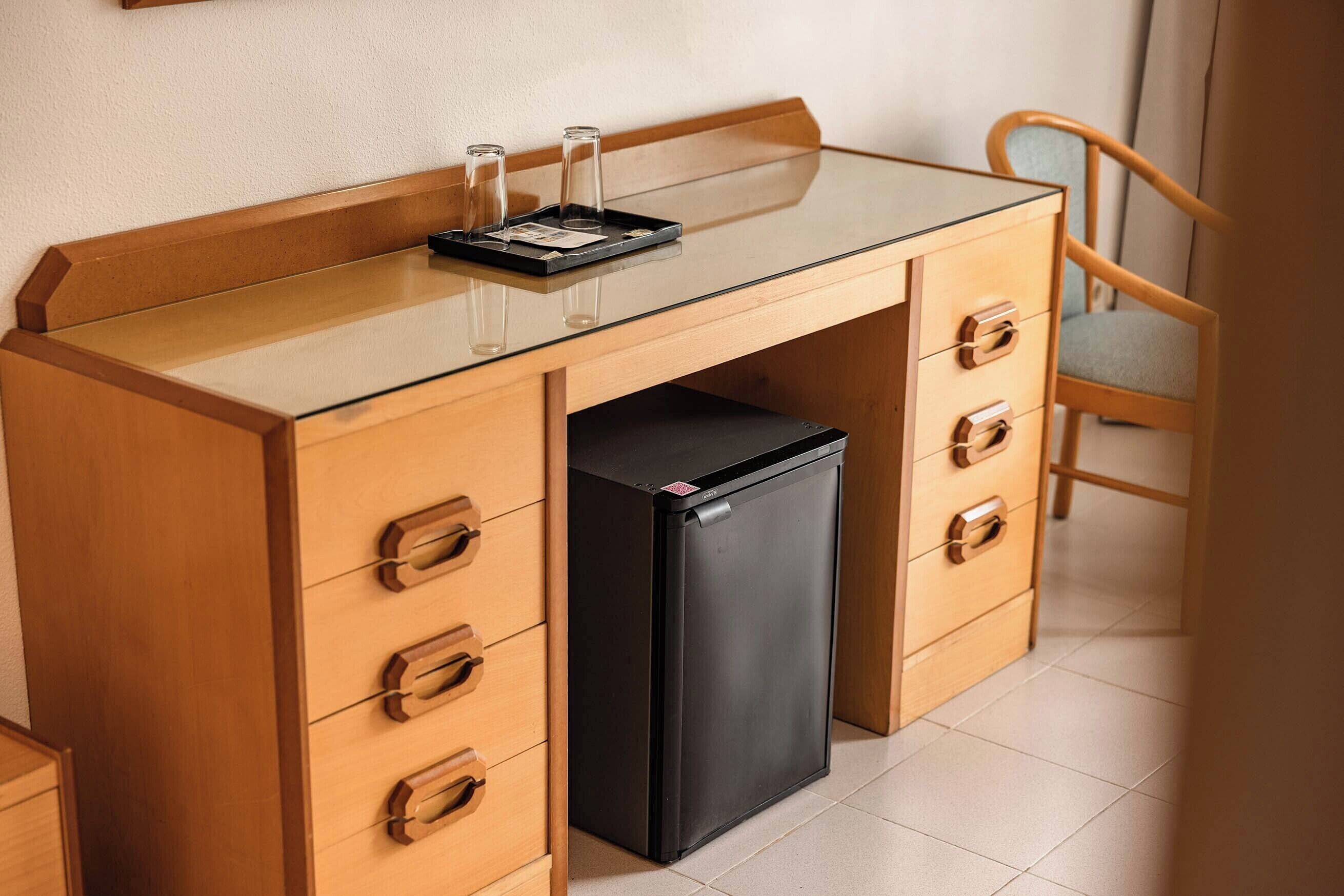Eine kleine Küche mit einer Esstischplatte aus Glas, einem schwarzen Kühlschrank und Holzschränken.
