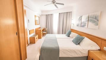 Habitación de hotel con dos camas, un escritorio, una silla, un armario y un ventilador de techo.