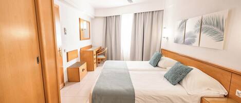Habitación de hotel con dos camas, un escritorio, una silla, un armario y un ventilador de techo.