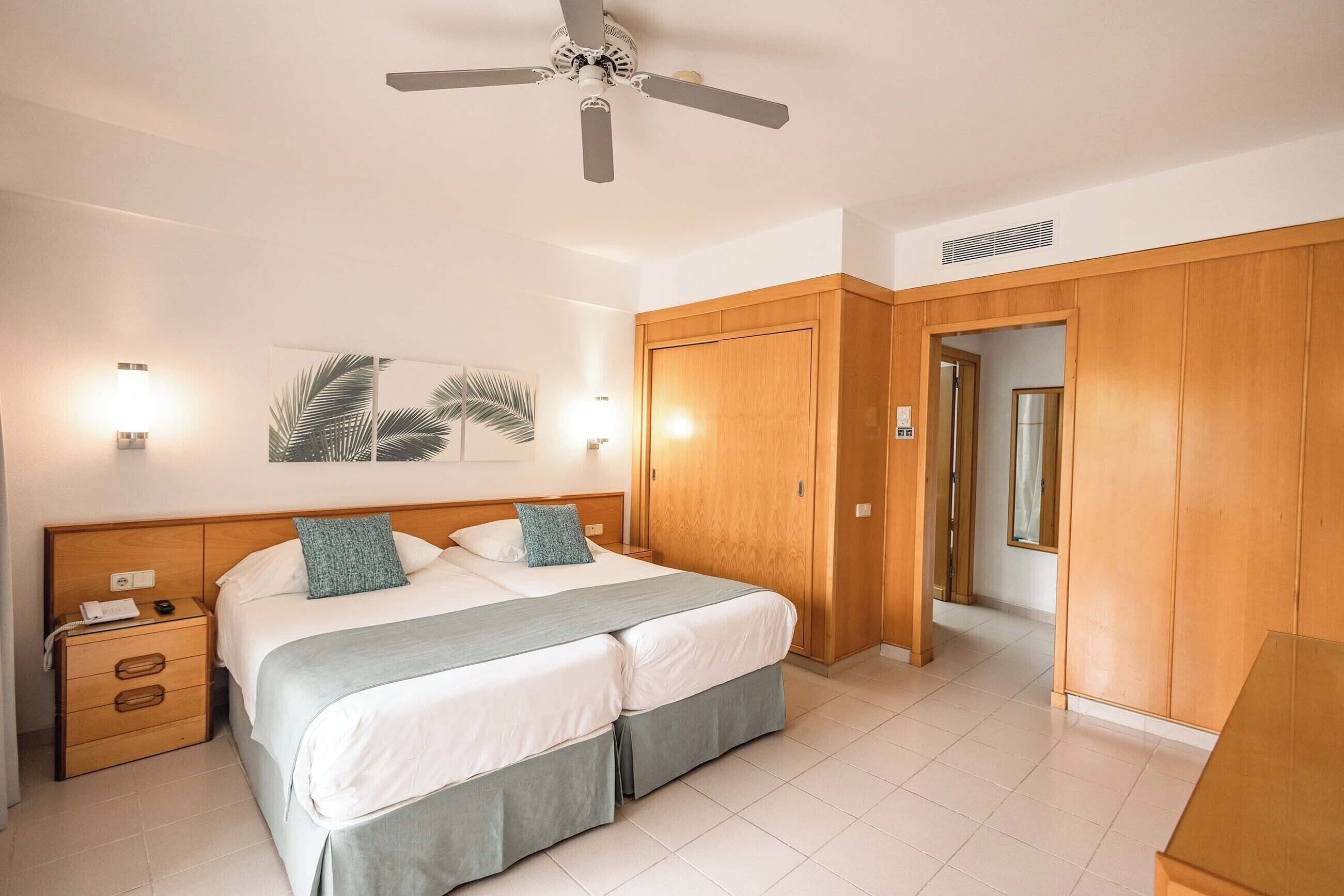 A hotel room with a bed, bedside table, lamp, and a ceiling fan.