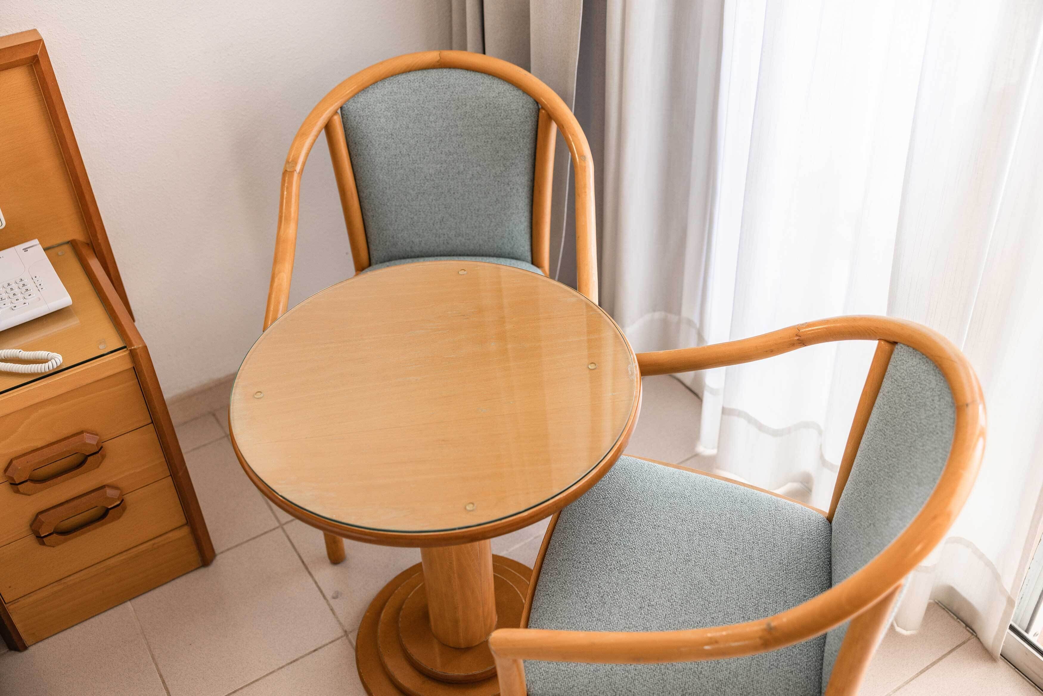 A wooden table with a glass top and two chairs with wooden frames and blue fabric seats.