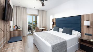 Una habitación de hotel moderna con una cama grande, un ventilador de techo, un televisor de pantalla plana, un escritorio con lámpara y vistas al exterior.