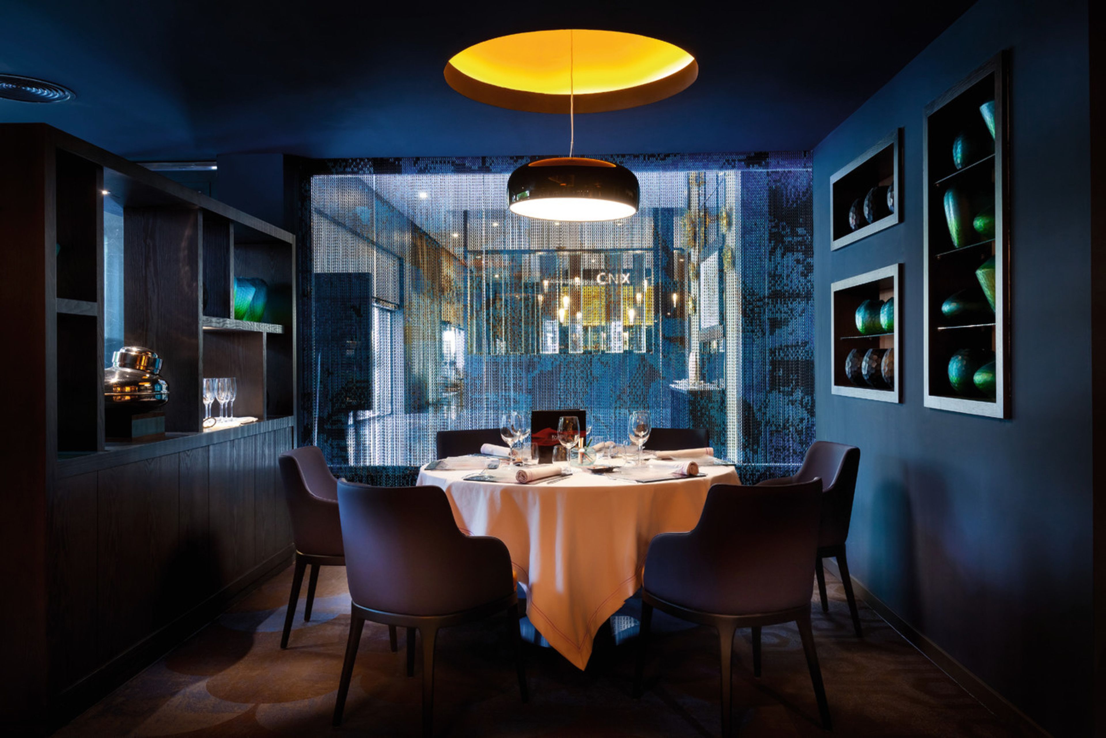Un comedor moderno con una mesa redonda, sillas, una araña y una pared decorada con cuadros.