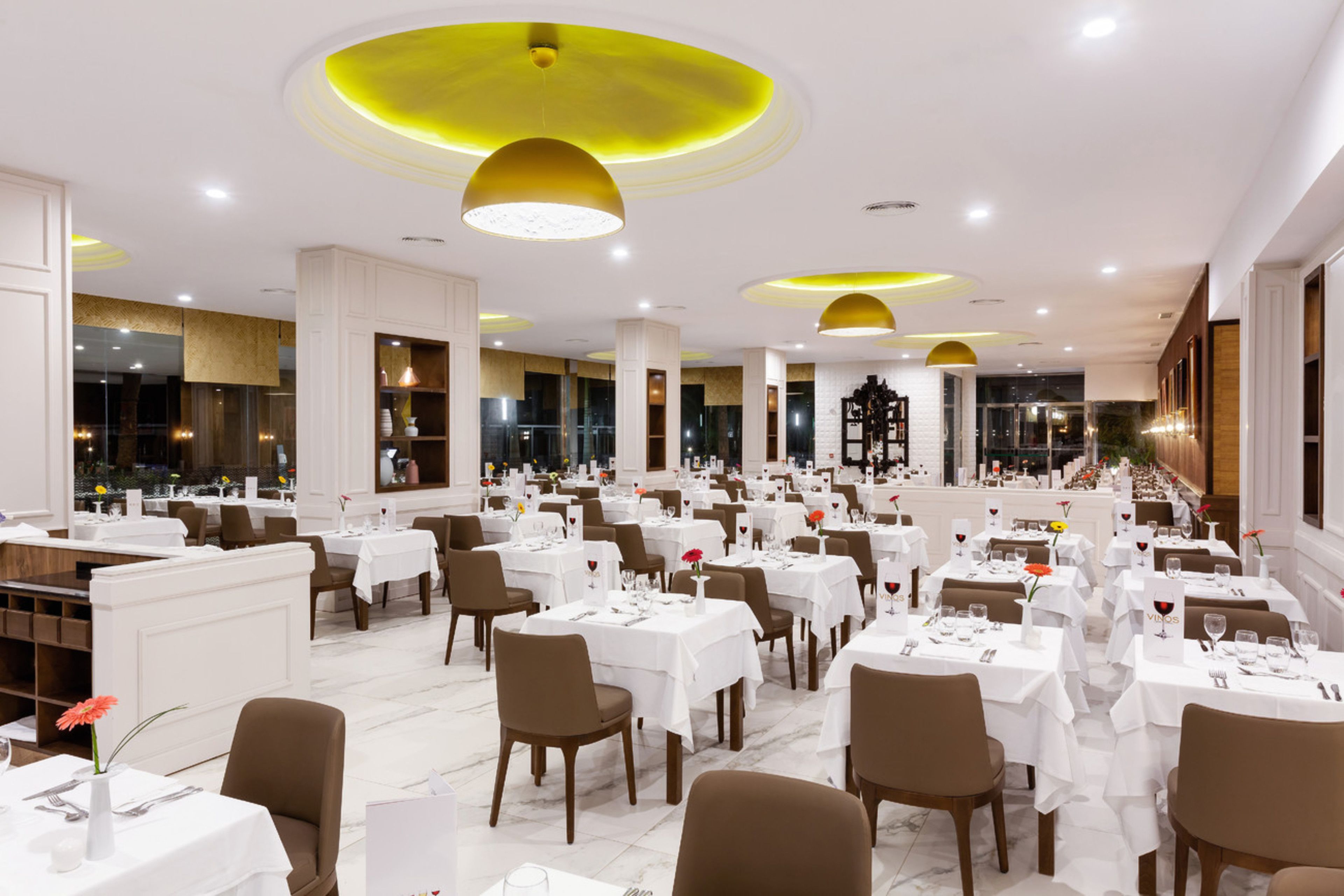 Un comedor amplio con varias mesas y sillas, bien iluminado por luces del techo.