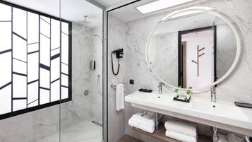 Un baño moderno con ducha de vidrio, un espejo grande y un tocador blanco con toallero.