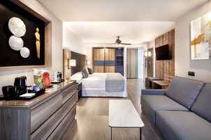 A modern hotel room with a bed, a sofa, a desk with a coffee maker, a TV, and artwork on the walls.