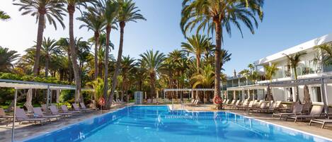 Una piscina con sillones de descanso y palmeras.