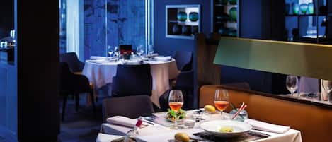 A restaurant with tables set for dining, a bar area, and a decorative wall with shelves.