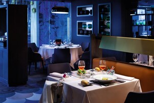 Restaurante com mesas preparadas para refeições, área de bar e parede decorativa com prateleiras.