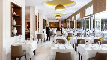 A restaurant with white tables, brown chairs, and a waiter.