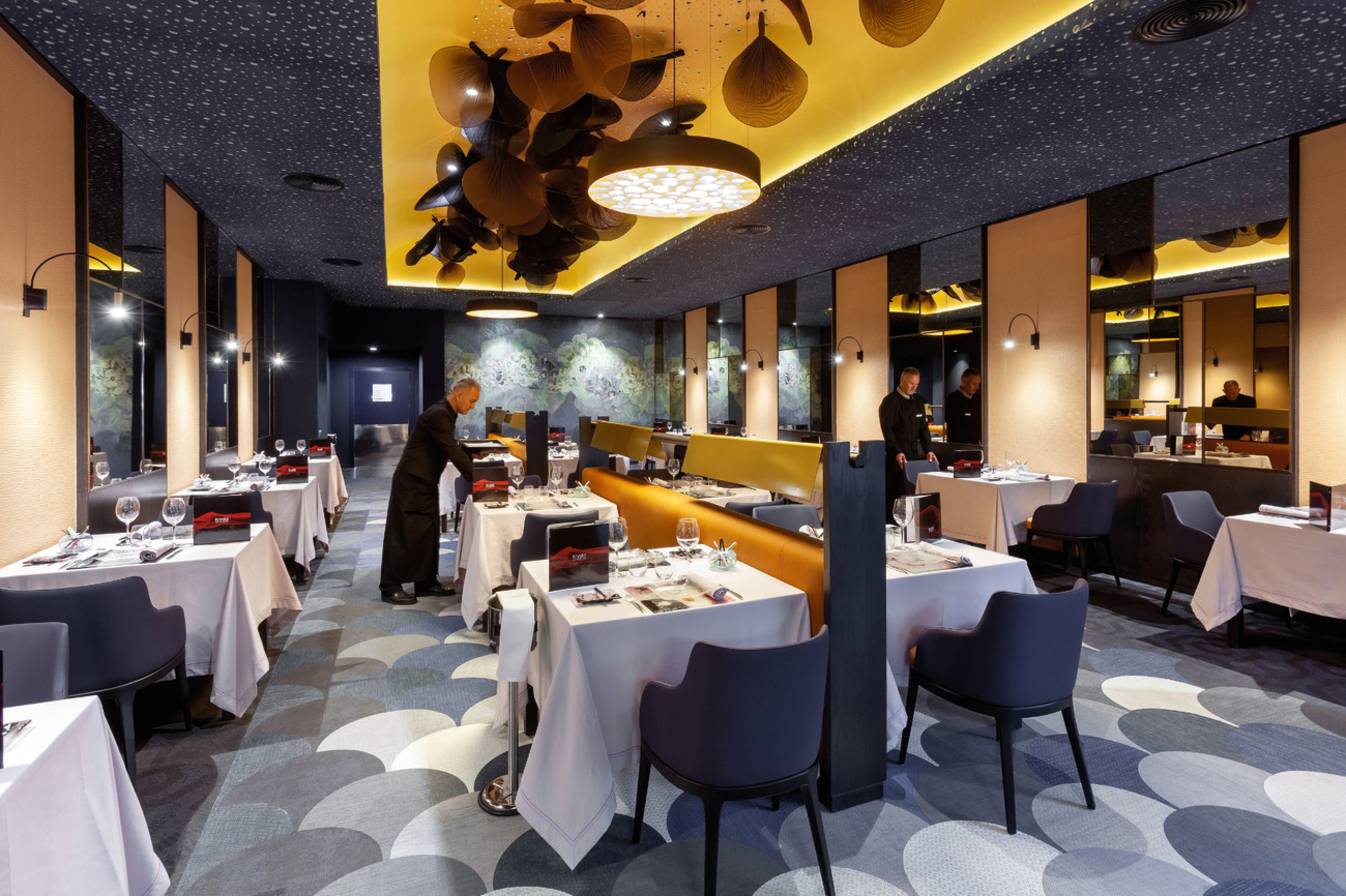 Un restaurant modern amb taules i caires, una zona de bar i una barra llarga.