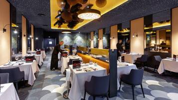 Un restaurant modern amb taules i caires, una zona de bar i una barra llarga.
