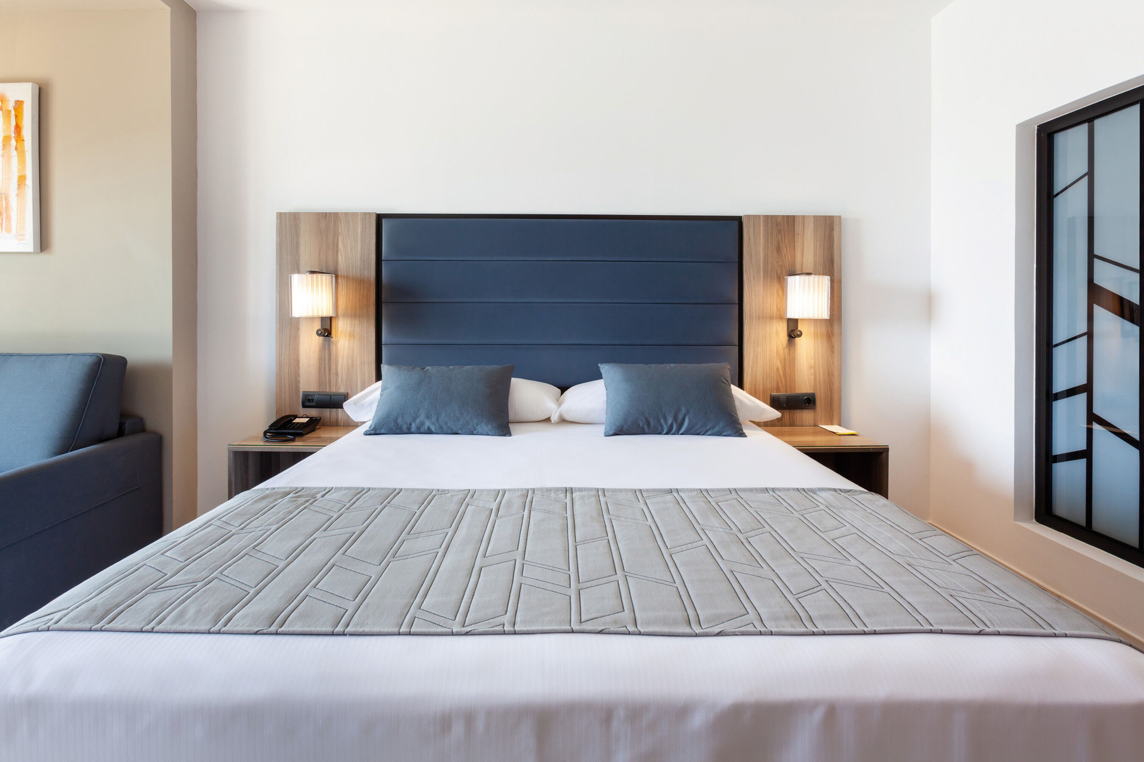 A hotel room with a large bed, two bedside tables, a nightstand, a chair, and a window with a view.