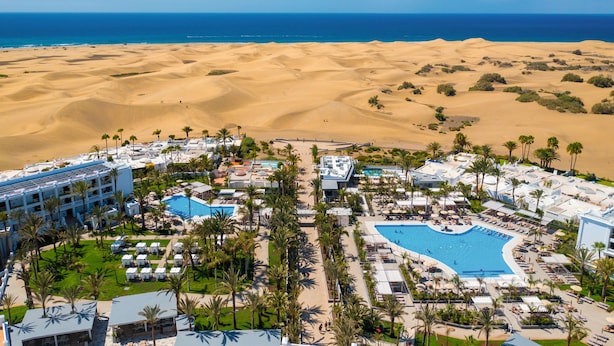 Un resort con una piscina grande, palmeras y un paisaje desértico de fondo.