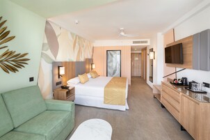 A hotel room with a bed, a green sofa, a desk with a TV, and a bathroom visible through an open door.