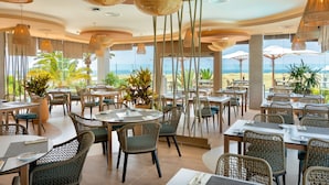 Un restaurante con mobiliario de mimbre, ventanas amplias y vistas a la playa.