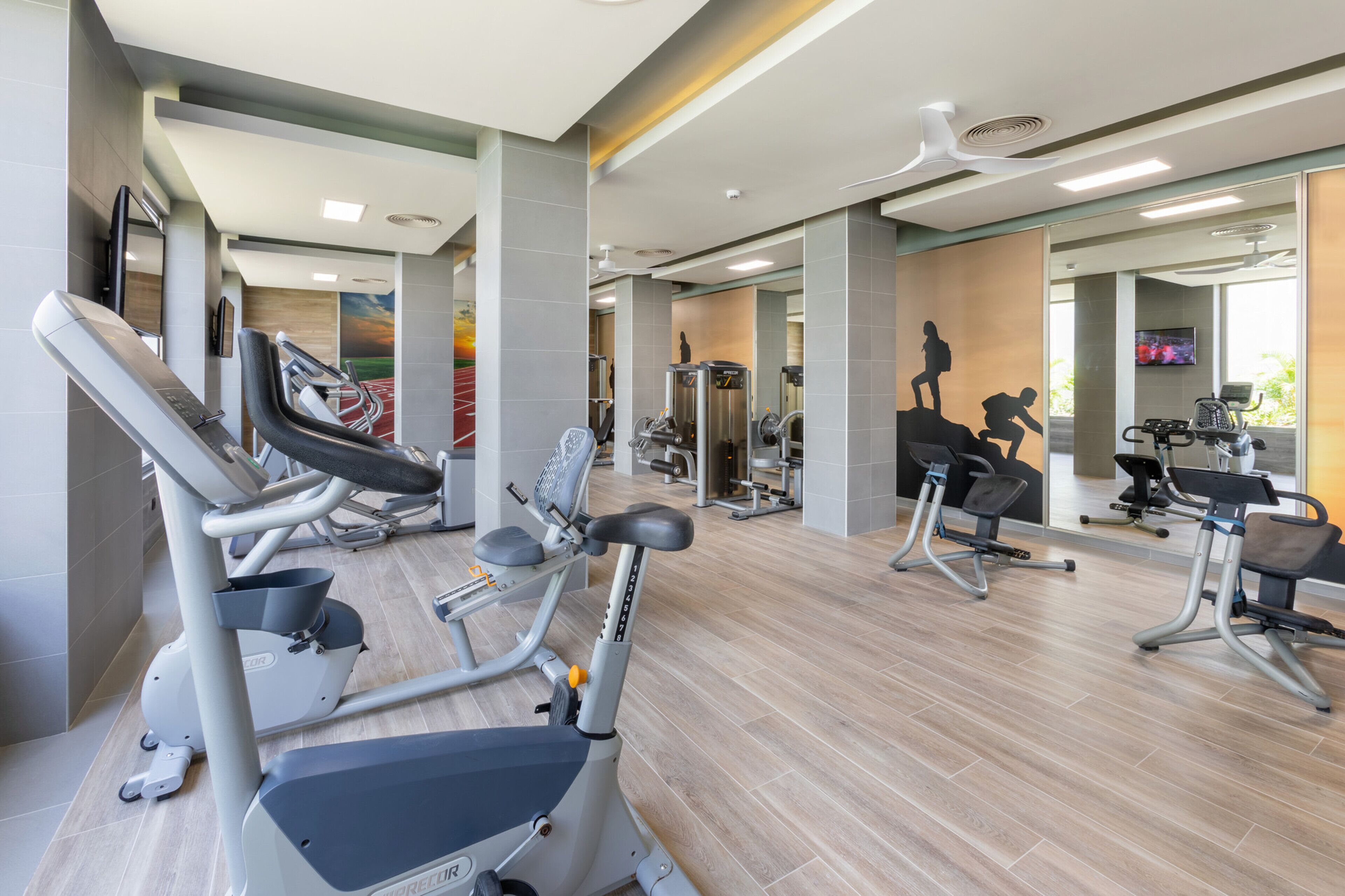 A modern gym with various exercise equipment, including treadmills and weight machines, and mirrors on the walls.