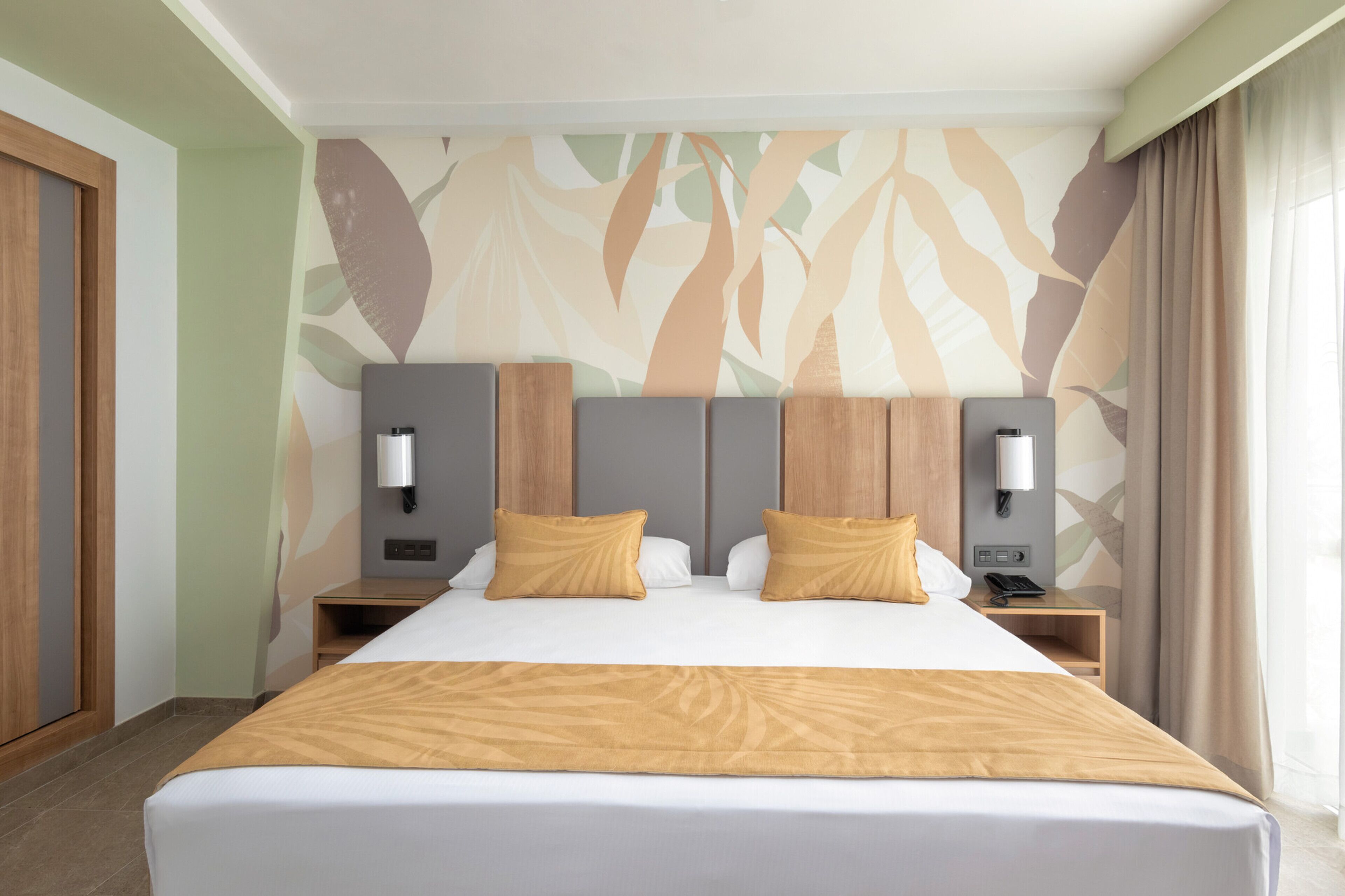 Habitación de hotel con una cama grande, dos mesitas de noche, un teléfono en la pared y un papel tapiz con estampado de hojas.